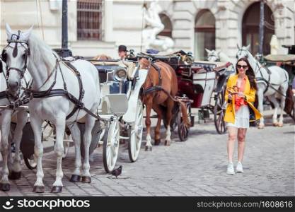 Happy woman walking in european street. Young attractive tourist outdoors in Vienna city on the piazza where a carriage with two horses runs. Woman walking in city. Young attractive tourist outdoors in italian city