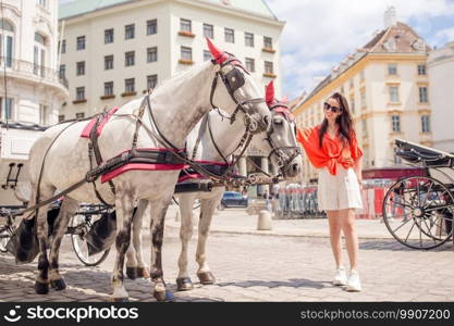 Happy woman walking in european street. Young attractive tourist outdoors in Vienna city on the piazza with two horses in carriage. Woman walking in city. Young attractive tourist outdoors in italian city