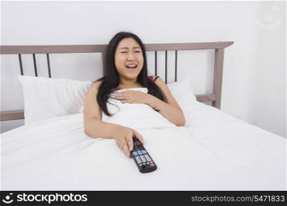 Happy woman watching TV in bed
