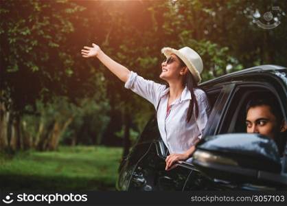 Happy woman waving hand outside open window car with her boyfriend on forest background. People lifestyle relaxing as traveler on road trip in holiday vacation. Transportation and weekend travel