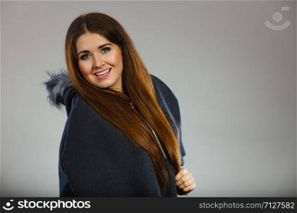 Happy woman wearing dark poncho coat with furry hood. Winter fashion, trendy clothing outfits concept.. Happy woman wearing dark poncho coat with hood