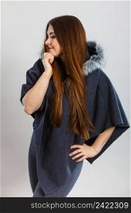 Happy woman wearing dark poncho with furry hood. Winter fashion, trendy clothing outfits concept.. Happy woman wearing dark poncho with hood