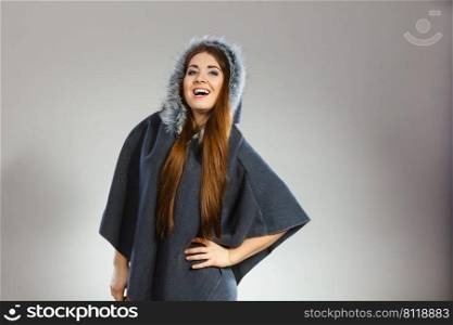 Happy woman wearing dark poncho with furry hood. Winter fashion, trendy clothing outfits concept.. Happy woman wearing dark poncho with hood