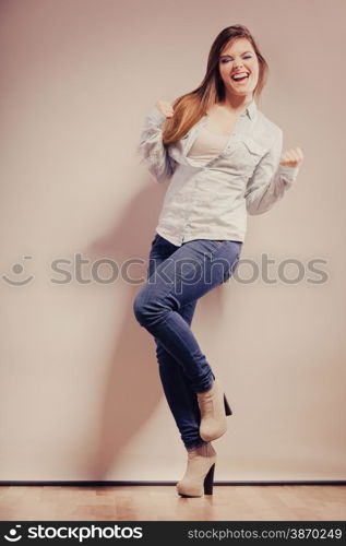 Happy woman wearing denim pants high heels. Girl in full length celebrating success clenching fist filtered photo