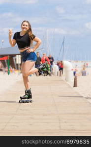 Happy woman wearing roller skates enjoying her free time while eating ice cream during summer sunny weather on beach. Roller skate woman eating ice cream