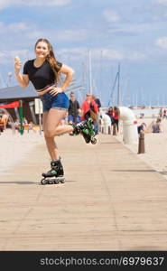 Happy woman wearing roller skates enjoying her free time while eating ice cream during summer sunny weather on beach. Roller skate woman eating ice cream