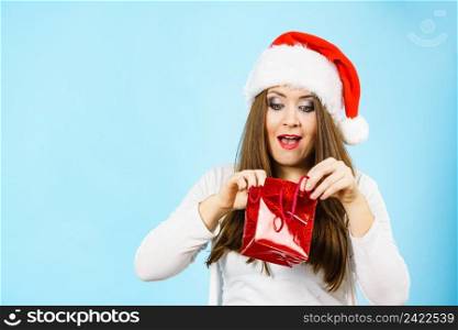 Happy woman wearing santa claus hat looks into christmas red gift bag, on blue. Christmas Woman looks into red gift bag