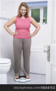 Happy Woman Weighing Herself On Scales In Bathroom