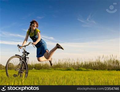 Happy woman  with a old bicycle in a green meadow and jumping