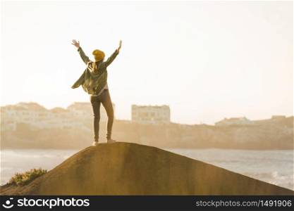 Happy woman with arms raised over the cliff seeing the beach