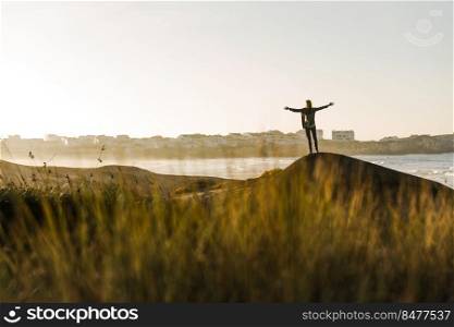 Happy woman with arms raised over the cliff seeing the beach