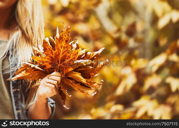 Happy woman with beautiful bouquet of a dry maple leaves in bright sunny day in autumn park, enjoying fall vacation