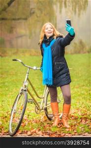 Happy woman with bike in park taking selfie photo.. Happy active woman with bike bicycle in fall autumn park taking selfie self photo picture. Glad young girl in jacket and scarf relaxing. Healthy lifestyle.