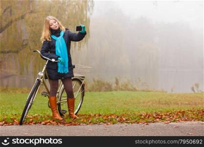Happy woman with bike in park taking selfie photo.. Happy active young woman girl with bike bicycle in fall autumn park taking selfie self photo picture.