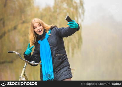 Happy woman with bike in park taking selfie photo.. Happy active woman with bike bicycle in fall autumn park taking selfie self photo picture. Glad young girl in jacket and scarf relaxing. Healthy lifestyle.