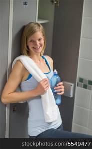 Happy woman with bottle and towel in locker room at healthclub
