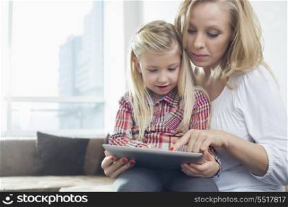 Happy woman with daughter using digital tablet in living room