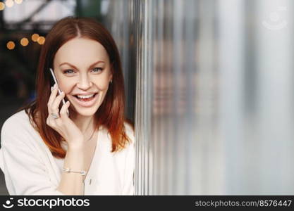 Happy woman with dyed hair, gets good news during conversation on cell phone, discusses latest news in business sphere, laughs joyfully, talks on cellular, dressed in formal clothes. Technology