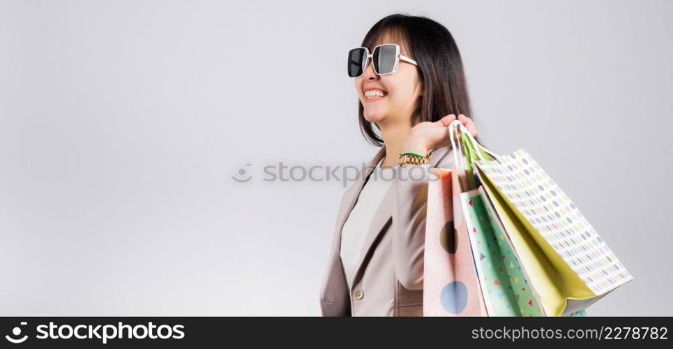 Happy woman with glasses confident shopper smiling holding online shopping bags colorful multicolor, Portrait excited Asian young female purchase studio shot isolated on white background, fashion sale