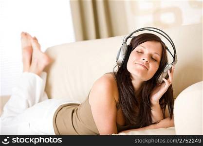 Happy woman with headphones lying down on sofa in lounge, listen to music