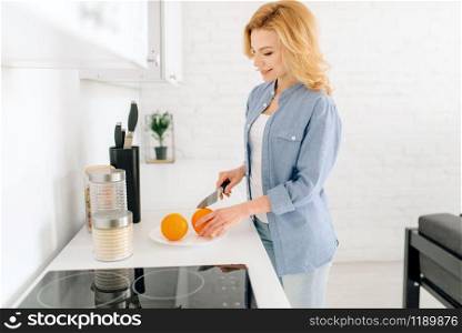Happy woman with knife preparing oranges, breakfast on the kitchen. Female person at home in the morning, healthy nutrition and lifestyle