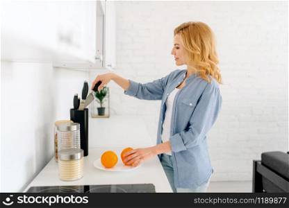 Happy woman with knife preparing oranges, breakfast on the kitchen. Female person at home in the morning, healthy nutrition and lifestyle. Woman preparing oranges, breakfast on the kitchen