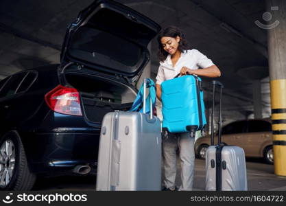 Happy woman with many suitcases in car parking. Female traveler with luggage in vehicle park lot, passenger with bag. Girl with baggage near automobile. Happy woman with many suitcases in car parking