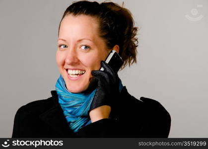 happy woman with mobile phone in black coat on gray background