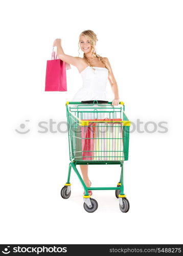 happy woman with shopping bags and cart over white