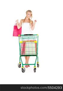 happy woman with shopping bags and cart over white