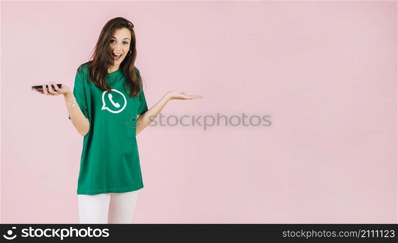 happy woman with smartphone shrugging pink backdrop