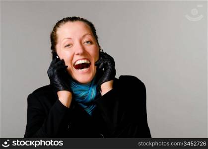 happy woman with two mobile phones in black coat on gray background