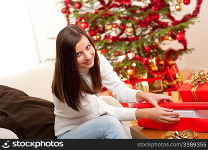 Happy woman wrapping Christmas present in front of tree