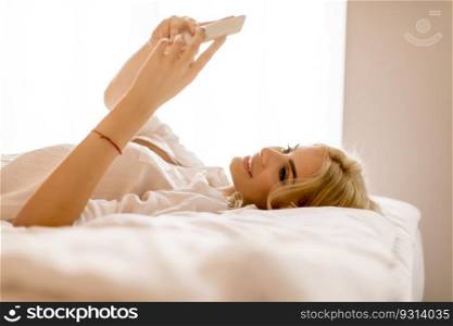 Happy womanl using a mobile phone lying on the bed at home