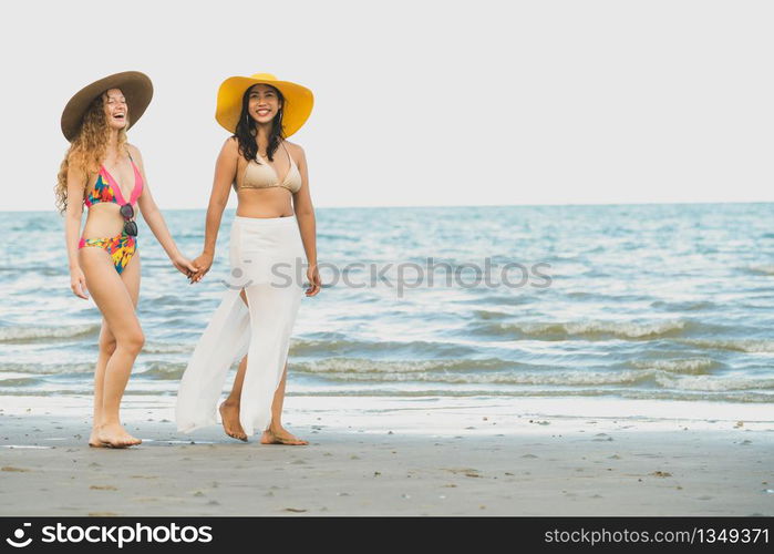 Happy women in bikinis go sunbathing together on tropical sand beach in summer vacation. Travel lifestyle.. Happy women go sunbathing at sand beach in summer.