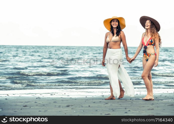 Happy women in bikinis go sunbathing together on tropical sand beach in summer vacation. Travel lifestyle.. Happy women go sunbathing at sand beach in summer.