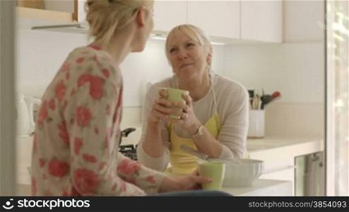 Happy women in home kitchen, mom and daughter talking and drinking a cup of tea