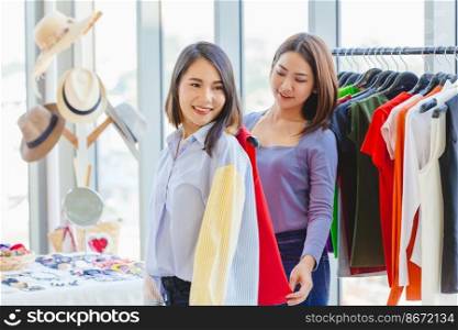 happy women shopping with friend in fashion shop for select new colorful clothes and measure size at shoulder.