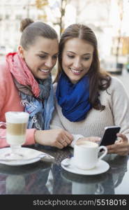 Happy women using cell phone at sidewalk cafe