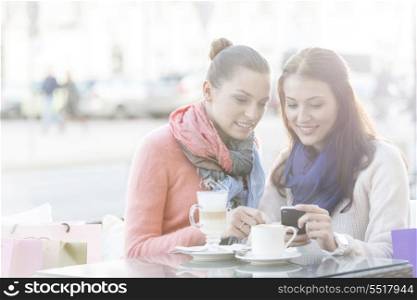 Happy women using cell phone at sidewalk cafe during winter