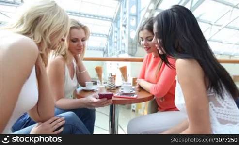 Happy women with smartphones talking in cafe after shopping in mall