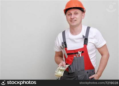 Happy worker in red uniform, protective hard hat holding bundle of dollars, cash money on white background. Male worker for advertisement. labor day.. Happy worker in red uniform, protective hard hat holding bundle of dollars, cash money on white background. Male worker for advertisement. labor day
