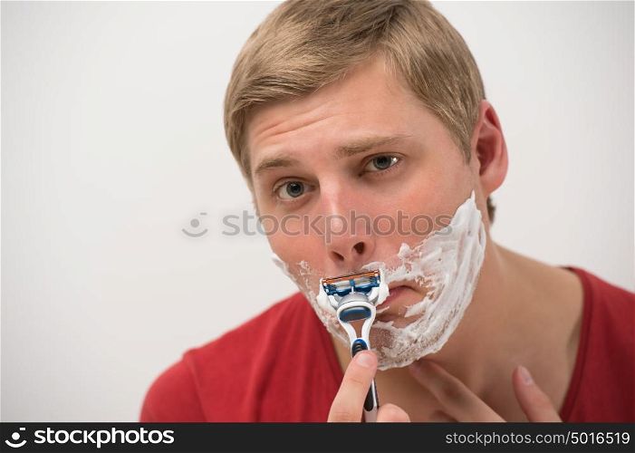 Happy young adult man shaving his face over white background