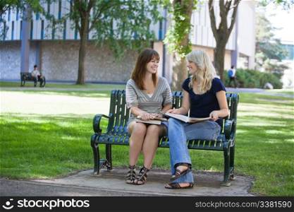 Happy young adults sitting on bench on college campus