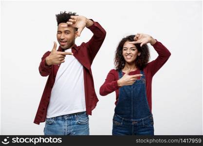 Happy young African American couple looking through a finger frame and smiling while standing isolated on white. Happy young African American couple looking through a finger frame and smiling while standing isolated on white.