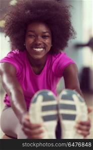 happy young african american woman in a gym stretching and warming up before workout. woman in a gym stretching and warming up before workout