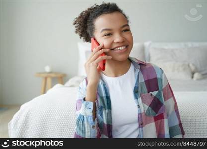 Happy young african american woman making phone call at home, smiling friendly biracial teen girl holding smartphone enjoying mobile conversation with friend, talking in bedroom.. Smiling young african american teen girl making phone call, talking with friend in bedroom at home
