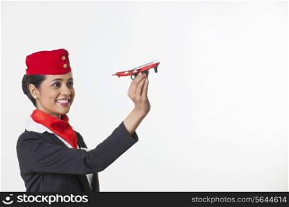 Happy young airhostess looking at toy airplane isolated over white background