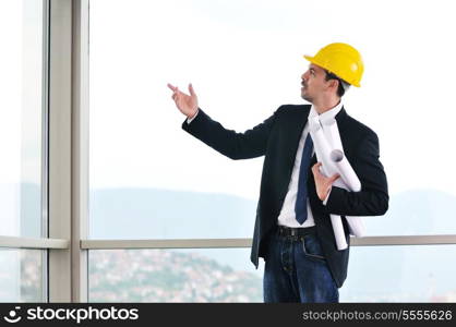 happy young architect portrait with helmet and blueprints indoor at new big bright appartment and construction site