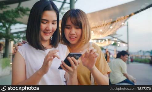 Happy young Asia women tourist with casual style look at photo on smartphone screen on mobile phone with river view sunset near cafe in city town at night. Lifestyle tourist travel holiday concept.